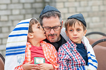 Two boys sit on their father's lap, one kisses his father on the cheek. Links to Gifts from Retirement Plans Two boys sit on their father's lap, one kisses his father on the cheek. Links to Gifts from Retirement Plans