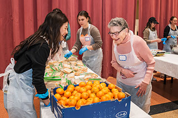 Two women laugh as they prepare a food table for an event together. Links to Gifts of Cash, Checks, and Credit Cards