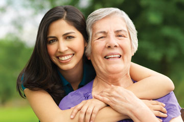 A woman hugging her grandmother from behind. Links to Gifts of Real Estate