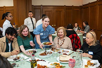 A table of people grin as a volunteer brings food to the table. Links to Closely Held Business Stock